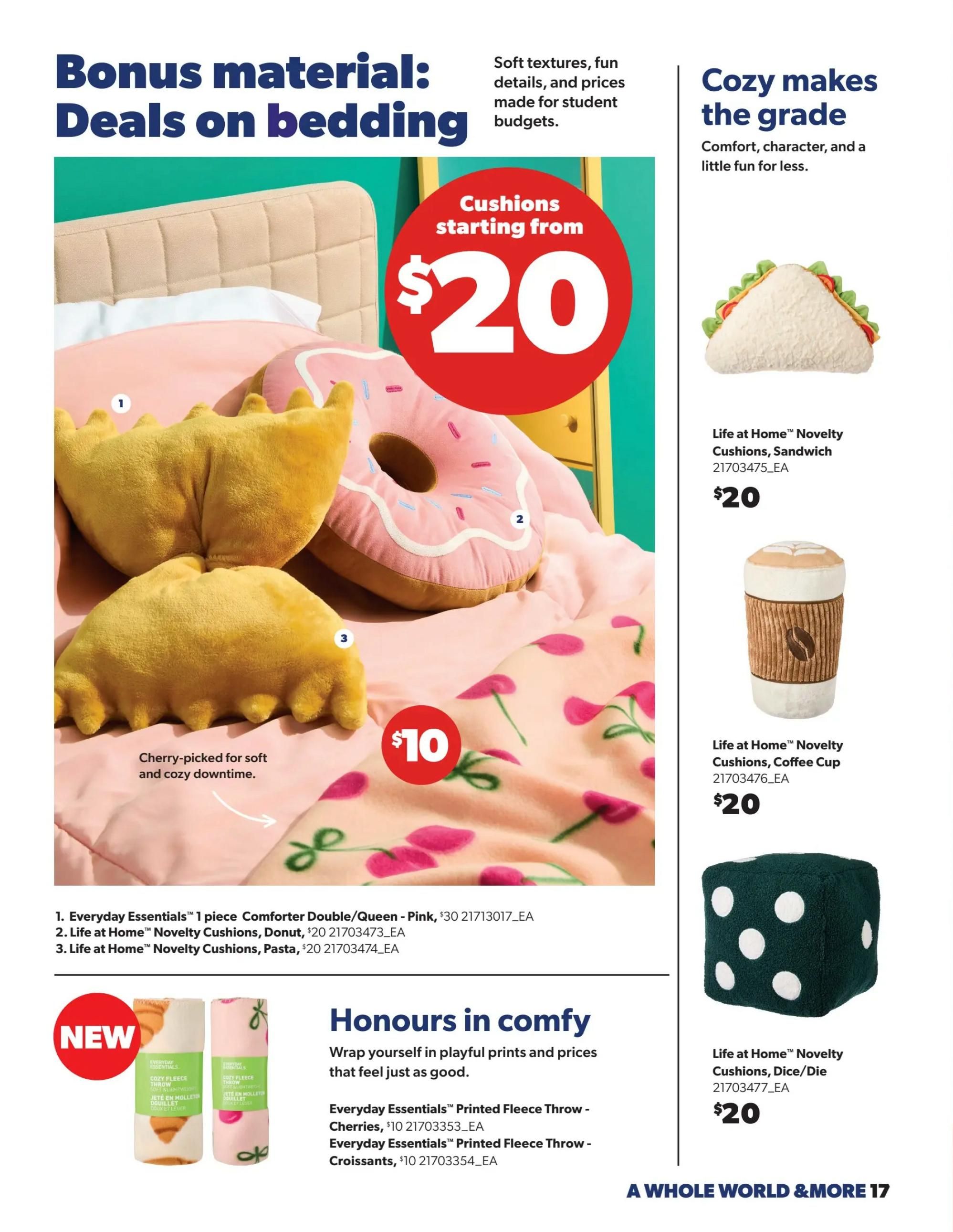 Real Canadian Superstore flyer page featuring 'Bonus material: Deals on bedding' and 'Cozy makes the grade'. The page highlights various cushions and throws. Featured items include Life at Home™ Novelty Cushions in Sandwich, Coffee Cup, and Dice/Die designs, all priced at $20 each. A large graphic advertises 'Cushions starting from $20'. Also shown are Everyday Essentials™ 1 piece Comforter Double/Queen in Pink for $30, and novelty cushions like Donut and Pasta for $20. New arrivals include Everyday Essentials™ Printed Fleece Throws in Cherries and Croissants patterns, both priced at $10. The page also mentions 'Honours in comfy' with playful prints and prices.